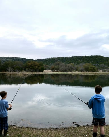 Two boys fishing from a dock with Hill Country hills in the background