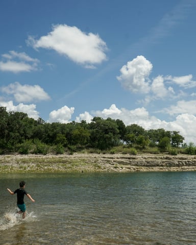 Child splashing in rocky Texas lake shallows on a sunny day