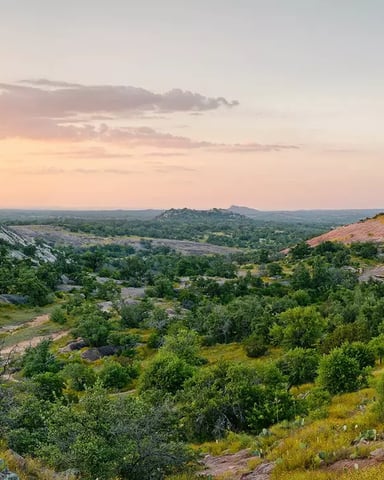 Panoramic view of Enchanted Rock at sunset with granite domes, scrub oak, and cactus stretching across the Hill Country