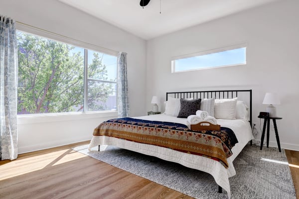 Urban bedroom with bright windows, fresh white linens, and a tray of folded towels